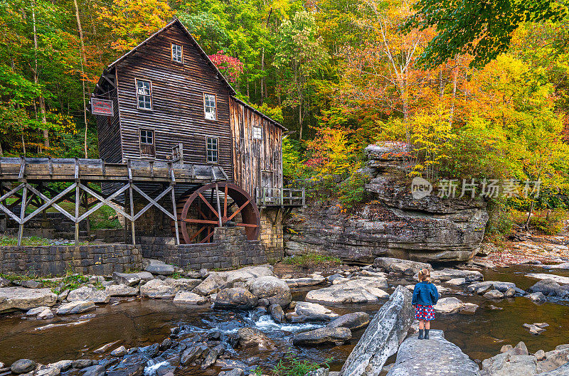 在美国西弗吉尼亚州阿巴拉契亚山脉的秋季，小女孩在巴布科克州立公园探索Glade Creek Grist磨坊。